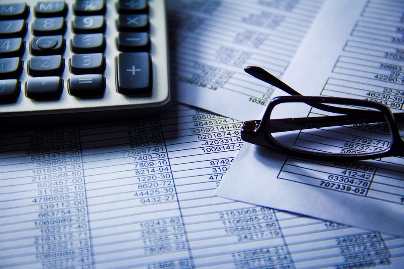 Budget and Finance Paperwork, Calculator sitting on top of paperwork and reading glasses. 