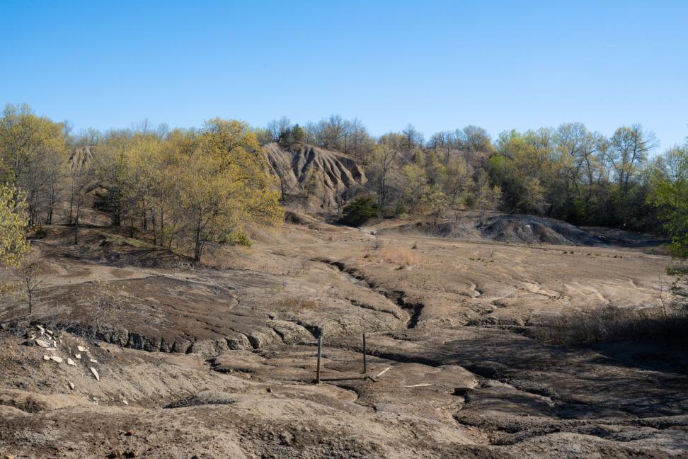 A barren spoil pile surrounded by trees and blue sky