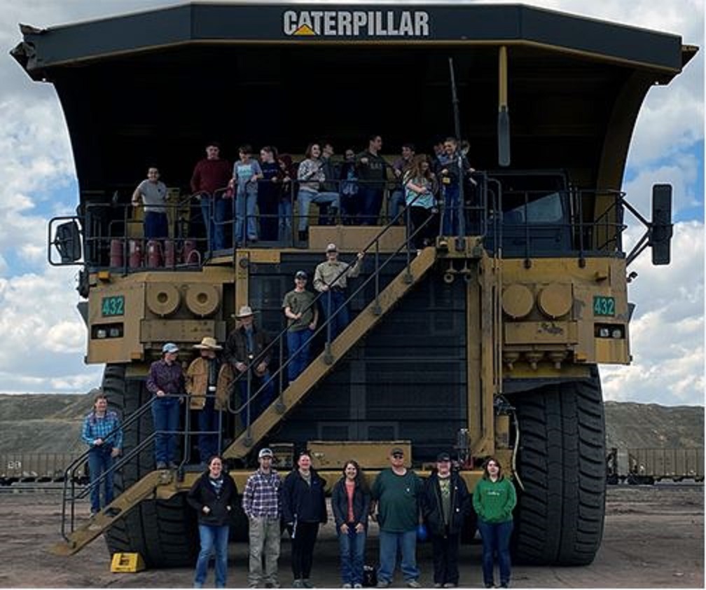 A group of people stand in front of and on a large piece of Caterpillar heavy equipment