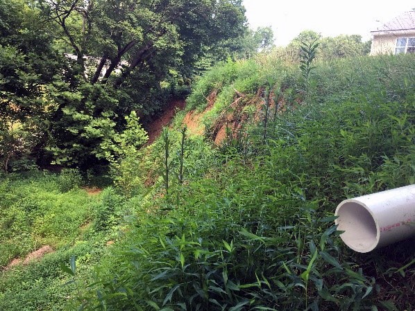 A grassy, subsided hillside with a white pipe in the foreground