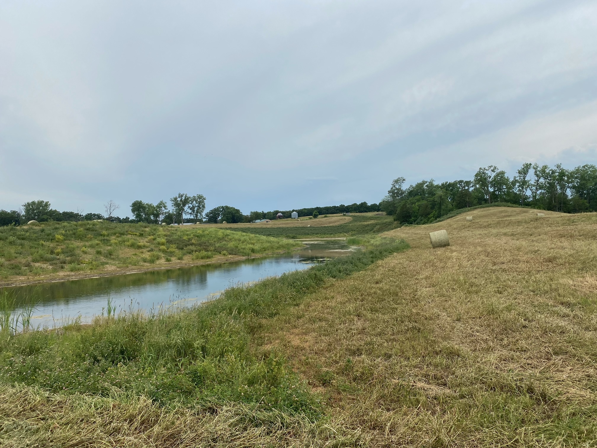 A stream runs through hills with hay bales.