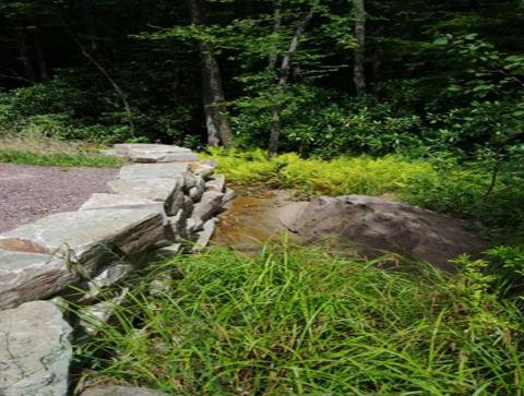 A rock wall and green vegetation surround the sloping land of an abandoned mine area