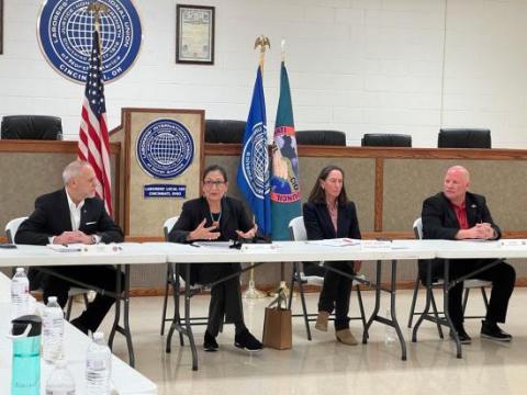 Secretary Haaland sits at a long white table with three other officials